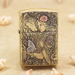 Brass lighter with an intricate engraved scene of a woman, a wolf, flowers, and a butterfly.