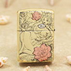 Gold decorative lighter featuring line-art of a reclining woman among pink flowers, on a metallic surface.