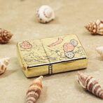 Gold-toned engraved lighter with floral design, placed on a sandy surface among seashells.