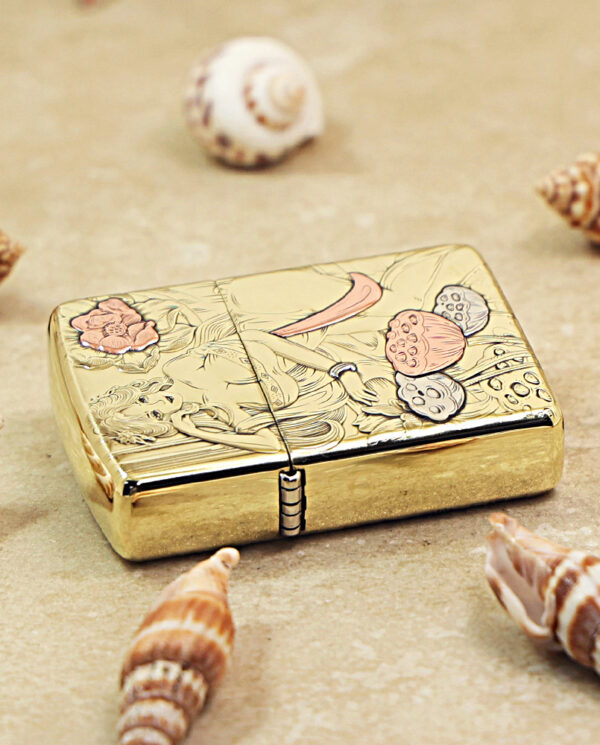 KZ456-04 Gold-toned engraved lighter with floral design, placed on a sandy surface among seashells.