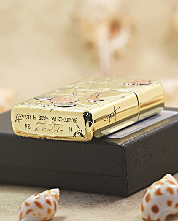 KZ456-05 Gold engraved Zippo lighter resting on a black rectangular box, surrounded by seashells in the foreground.