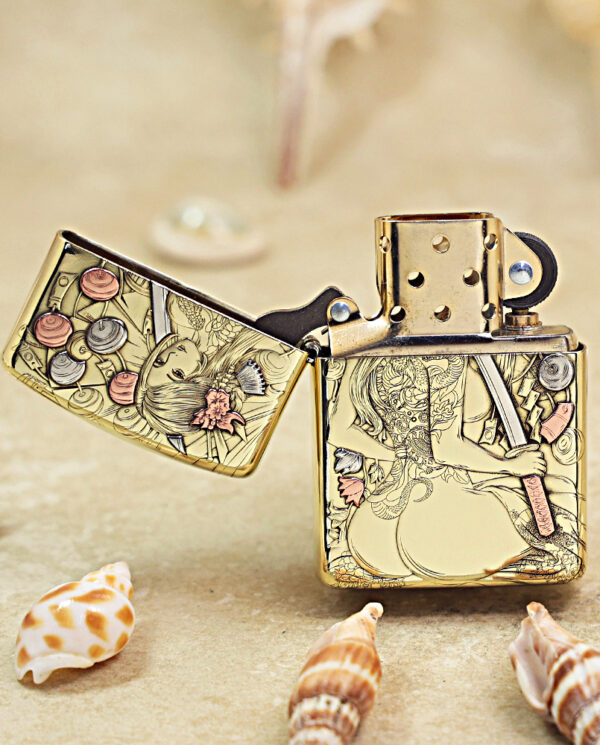 KZ457-02 Gold-tone Zippo-style lighter with intricate engraved artwork, open lid, resting on a sandy beach with seashells nearby