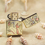 Gold-tone Zippo-style lighter with a pin-up girl engraving, open lid, resting on sand among seashells.
