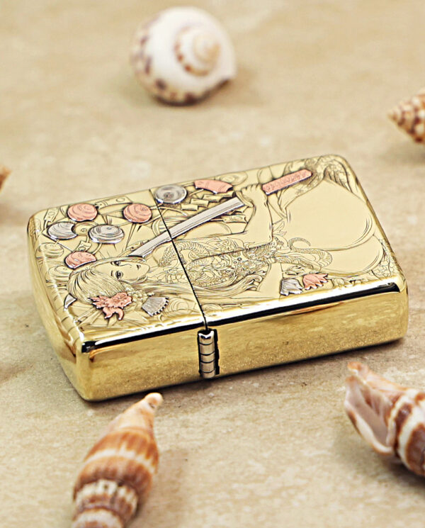 KZ457-04 Gold engraved lighter on a sandy surface with seashells around.