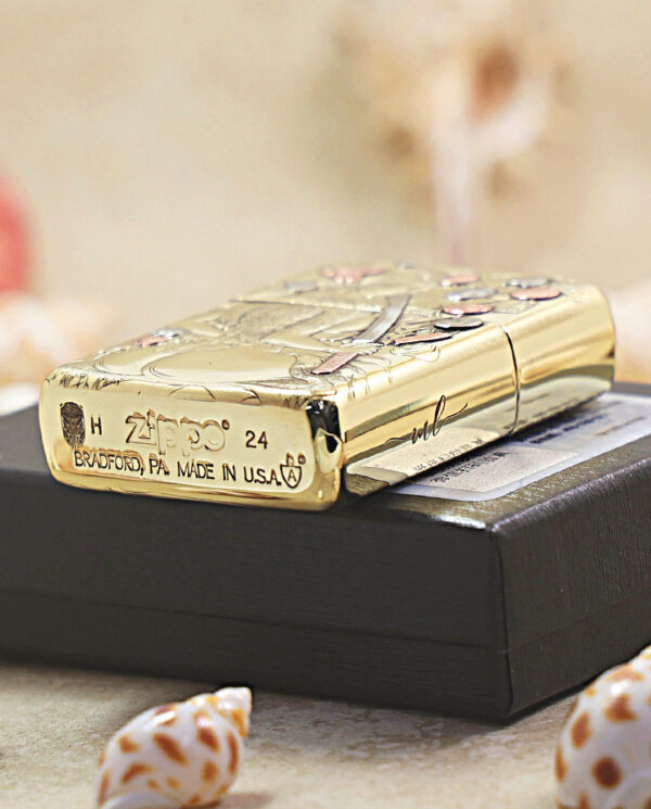 KZ457-05 Gold engraved Zippo lighter resting on a black display box, showing the 'Bradford, PA Made in USA' marking on the base.