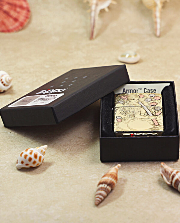 KZ457-06 Zippo lighter in armor case, black box open on a sandy beach with seashells scattered around, decorative engraving visible on the lighter edge.