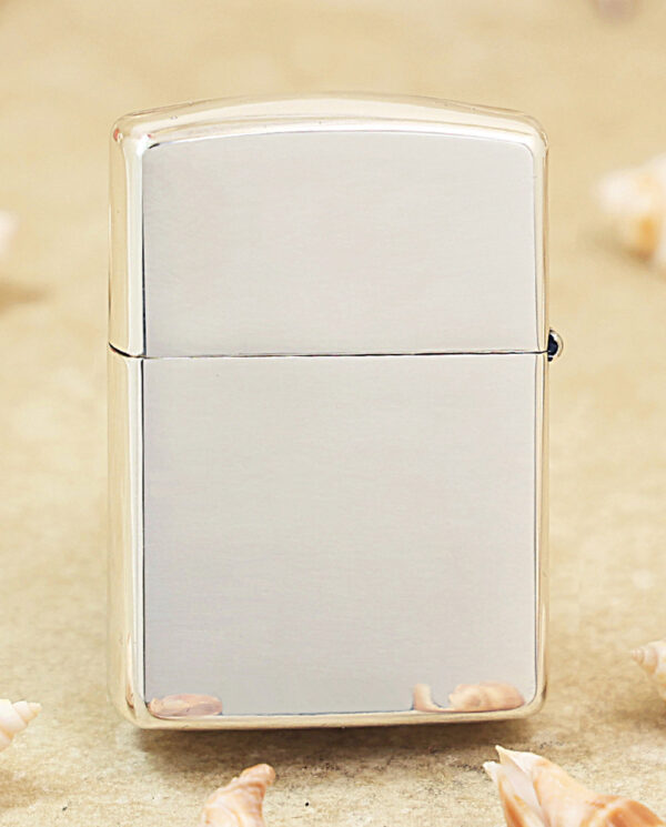 KZ461-01 Shiny metal Zippo-style lighter standing upright on sand, surrounded by seashells nearby.