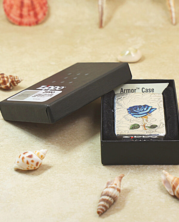KZ461-06 Zippo lighter with a blue rose design inside a black box on a sandy surface with seashells nearby; Armor Case label visible behind it.