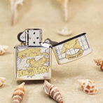 Open Tom and Jerry-themed Zippo lighter, metal case with cartoon panels resting on a sandy surface among seashells.