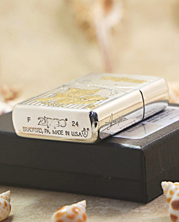 Shiny Zippo lighter resting on a black box with seashells around, showing engravings and 'Made in USA' text on the base