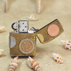 Novelty lighter wrapped in a map-pattern case with attached coins, resting on sandy beach with seashells nearby.