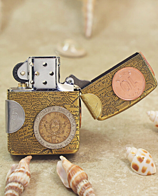 KZ468-03 Novelty lighter wrapped in a map-pattern case with attached coins, resting on sandy beach with seashells nearby.