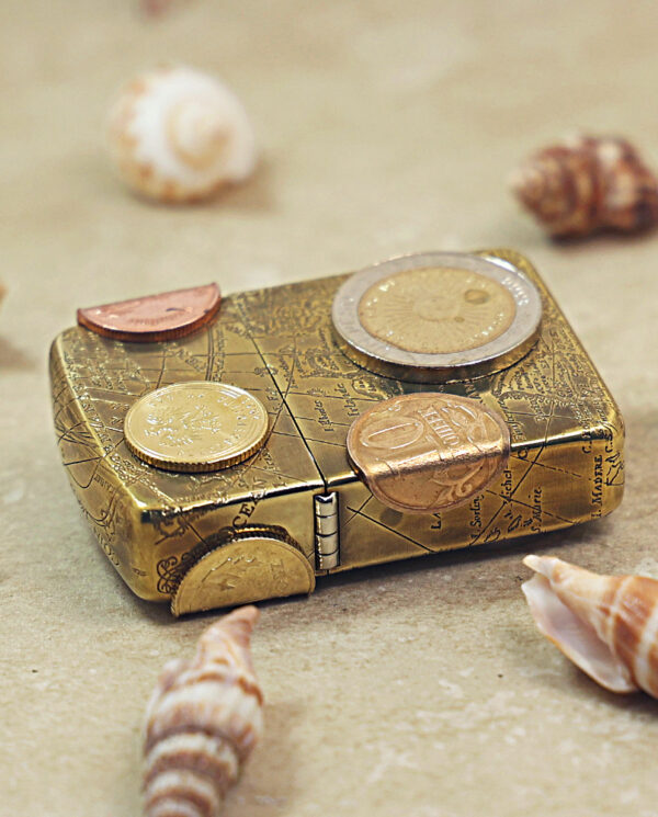 KZ468-04 Small decorative gold box with coins arranged on its lid, surrounded by seashells on a sandy surface.
