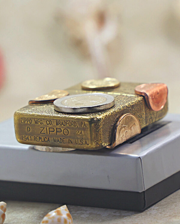 KZ468-05 Brass Zippo lighter with coins attached, resting on a gray gift box.