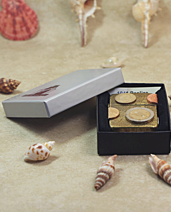 KZ468-06 Open black gift box revealing a money-themed trinket with coins on top, set among seashells on a sandy surface.