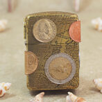 Travel-themed vintage lighter with a map engraving and several coins attached to its surface on a beige background.