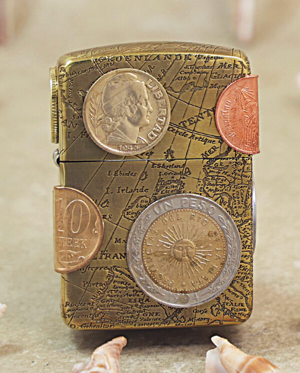KZ468 Travel-themed vintage lighter with a map engraving and several coins attached to its surface on a beige background.