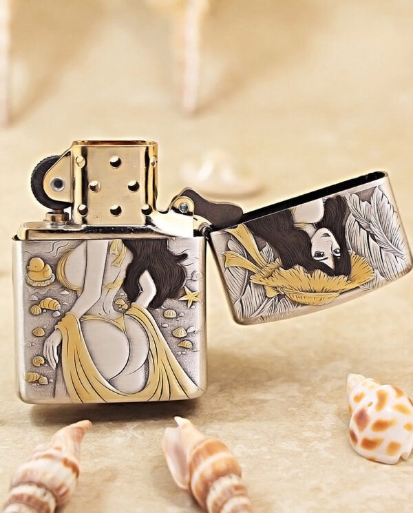 Ornate metal lighter with a mermaid-like illustration in yellow and black amid seashells on a sandy surface, surrounded by shells.