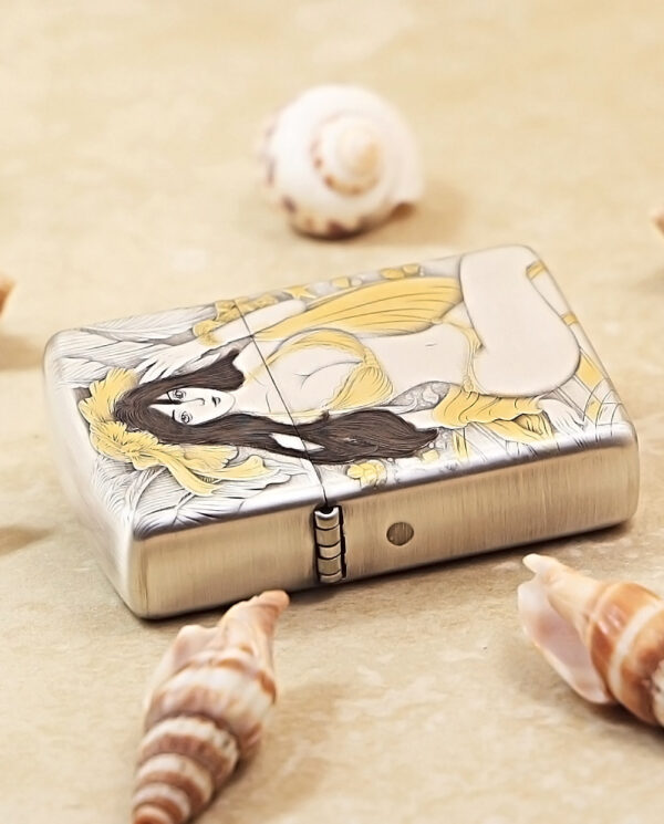 Metal lighter with a stylized illustration of a woman in yellow, surrounded by seashells on a sandy surface.