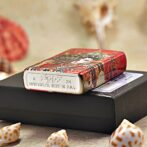 Decorative red Zippo lighter with ornate pattern resting on a black box; metal bottom shows 'Zippo' and 'Made in USA' (Bradford, PA).