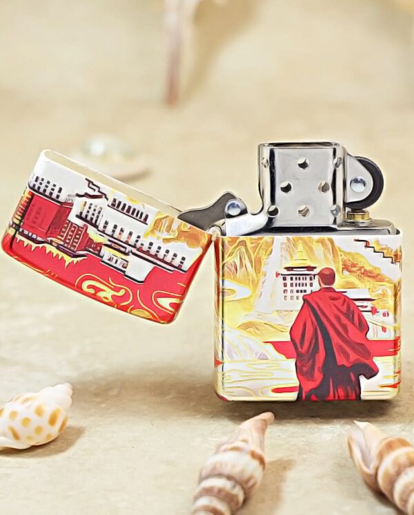 Colorful decorative lighter on sand, showing a red-cloaked traveler against a stylized landscape with seashells nearby.