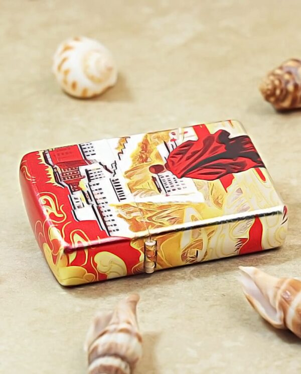 Decorative metal tin with red and gold Chinese motifs on a beige surface, surrounded by seashells.
