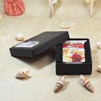 Open black gift box showing a colorful rectangular keepsake inside, with 'Made in USA' text, placed among seashells on a light surface.