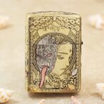 Golden ornate lighter featuring a split design: a dragon/ mask on one side and a serene woman’s profile, framed by circular patterns and script.