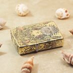 Ornate gold-engraved lighter on a sandy surface surrounded by seashells.