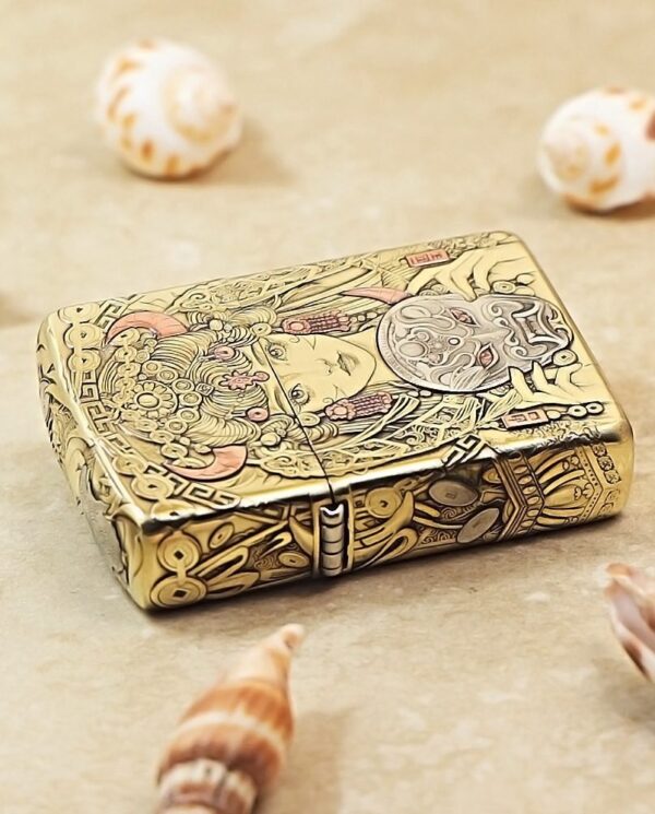 KZ501-04 Ornate gold-engraved lighter on a sandy surface surrounded by seashells.