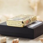 Decorative Zippo lighter with floral engravings resting on a black box; base reads Zippo, Bradford, PA, Made in USA and '24'.