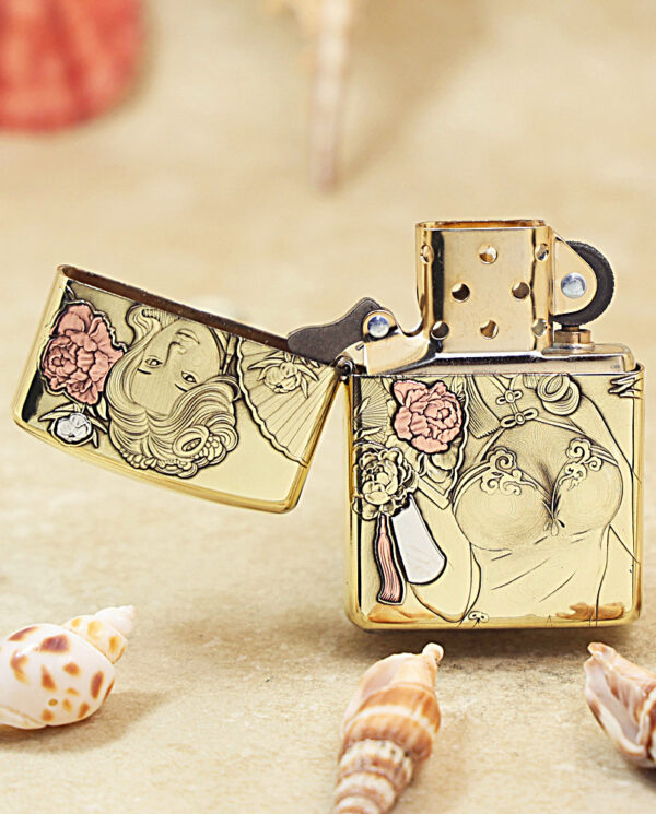 KZ506-02 Gold decorative Zippo lighter with floral and portrait design, lid open, placed on a sandy surface among seashells