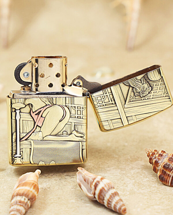 KZ506-03 Brass flip-top lighter with ornate engraved panels resting on sand among seashells.
