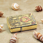 Gold-toned compact case with a raised engraving of a mermaid on the lid, surrounded by ornate detailing and small playing-card motifs nearby.