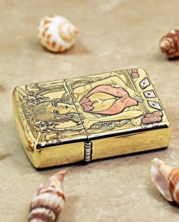 Gold-toned compact case with a raised engraving of a mermaid on the lid, surrounded by ornate detailing and small playing-card motifs nearby.