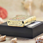 Gold Zippo lighter with decorative engravings resting on a black box, Bradford, PA, Made in USA visible on the side.