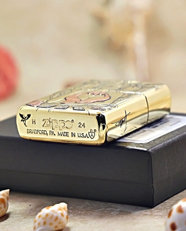 Gold Zippo lighter with decorative engravings resting on a black box, Bradford, PA, Made in USA visible on the side.