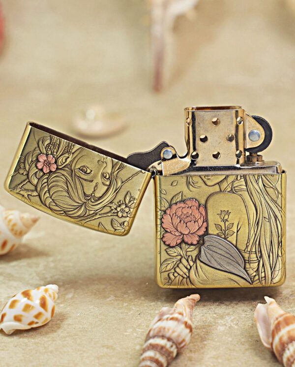 KZ509-02 Decorative brass lighter with floral engraving, open lid, on a sandy surface with seashells nearby.