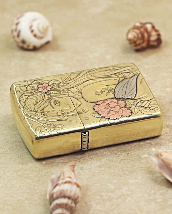 KZ509-04 Gold-toned compact with an engraved floral design and a woman's face, placed on sand among seashells