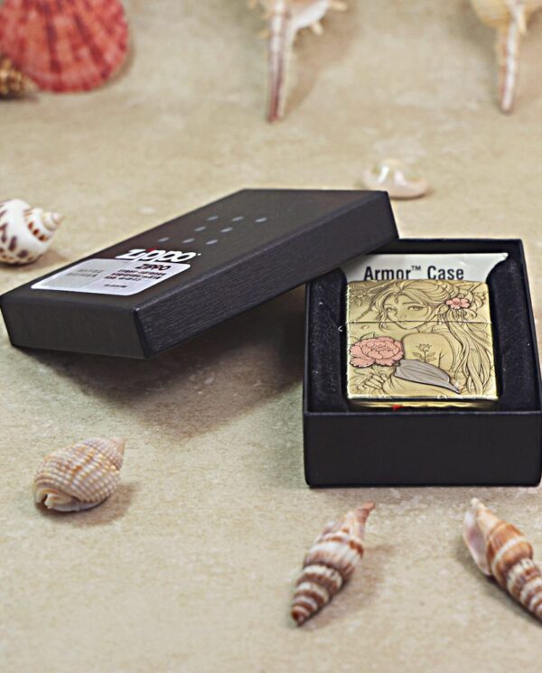 KZ509-06 Gold decorative Zippo lighter in a black presentation box, surrounded by seashells on a sandy surface.