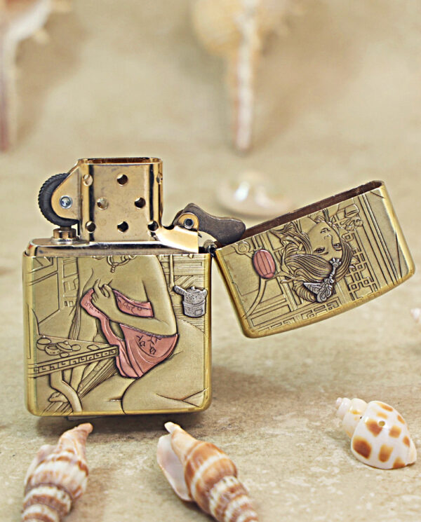 KZ510-03 Brass Zippo lighter with engraved Asian-style scenes, open lid, placed on a sandy surface among seashells.