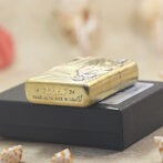 Gold Zippo lighter with a decorative pattern resting on a black box, showing 'ZIPPO' and 'Made in USA' engravings.