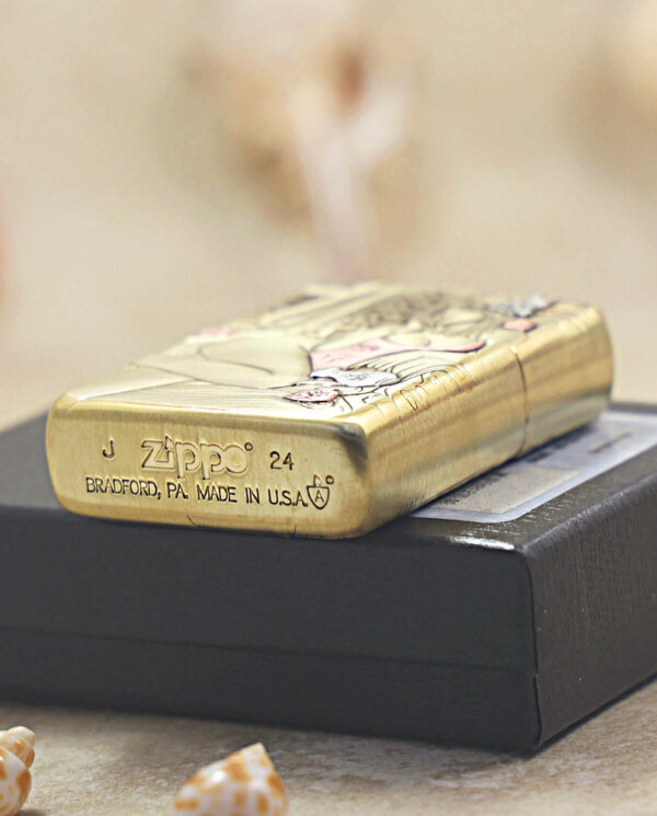 KZ510-05 Gold Zippo lighter with a decorative pattern resting on a black box, showing 'ZIPPO' and 'Made in USA' engravings.