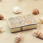 Silver lighter with an engraved mermaid and coral/starfish motif, set on a sandy surface among seashells.