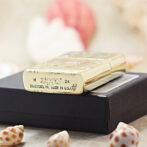 Gold Zippo lighter resting on a black box, surrounded by seashells in a soft-focus background.