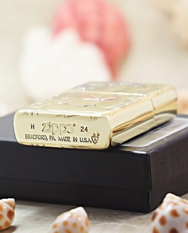 Gold Zippo lighter resting on a black box, surrounded by seashells in a soft-focus background.