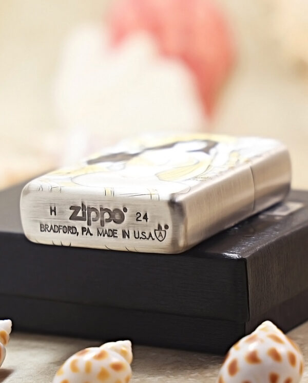 KZ370-05 Metal Zippo lighter resting on a black box, stamped with 'Zippo', 'Bradford, PA', 'Made in U.S.A.' and decorative design, with seashells nearby