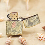 Gold engraved lighter with an open lid on a sandy surface, surrounded by seashells.