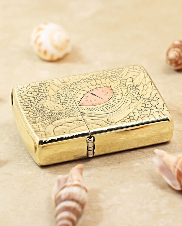 KZ371-04 Gold engraved lighter with a seashell motif, placed on a beige surface among small seashells.