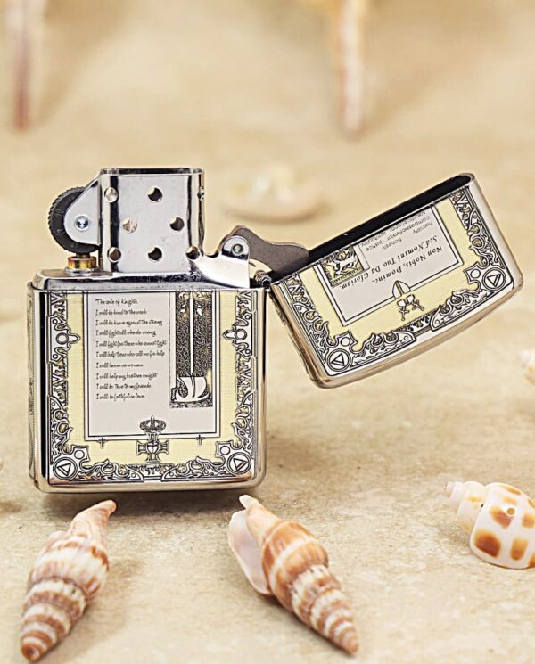 Metal lighter with ornate engraved pattern sits on sandy surface among seashells, open with the lid propped to the side.